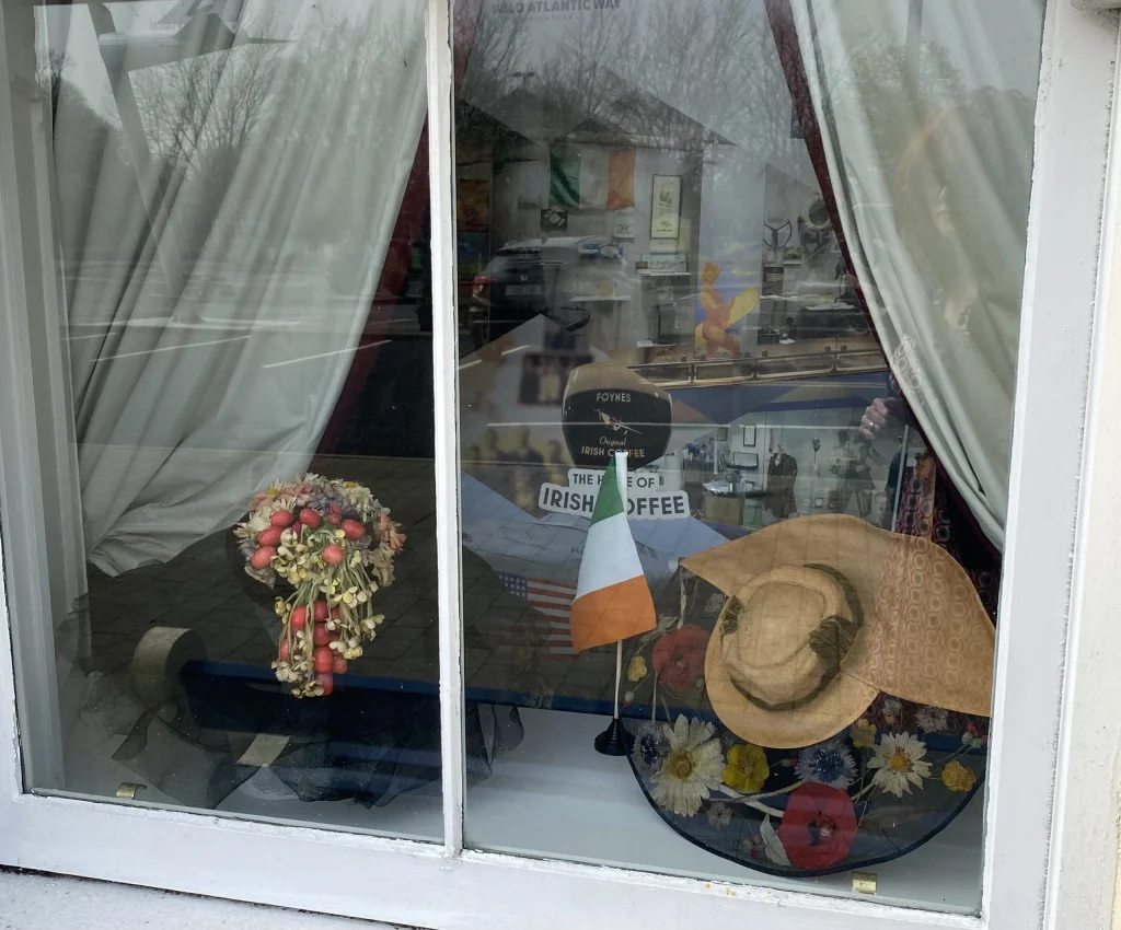 Second view of the O'Regans shop window showing vintage hats, a floral bonnet, and draped interior furnishings.